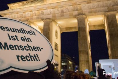 Eine Demonstration am Brandenburger Tor in Berlin, im Vordergrund ein Schild mit der Aufschrift "Gesundheit ist ein Menschenrecht"