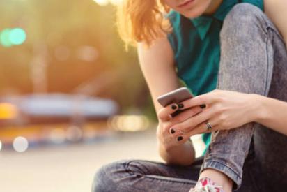 Person sitzt auf einer Mauer und tippt in ihr Smartphone.